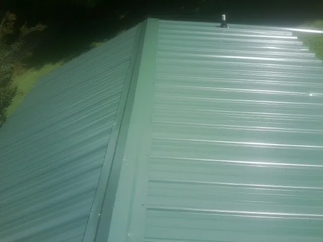 New green metal panels meeting at the ridge of a roof — Flat Roof Repair work by our crew in Carthage